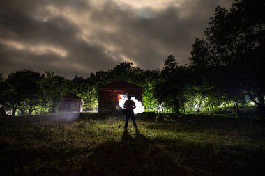 Adam gece ormanda silüeti. Işık ile karanlık ormanın içinde duran kişi silüeti. Karanlık gece ormanda. Gerçeküstü gece orman sahne. Korku Cadılar Bayramı kavramı.