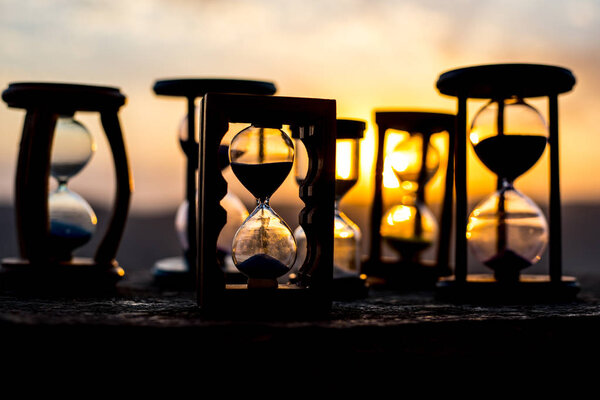 Hourglass Passing of Time Lapse Clouds. An hourglass in front of a bright blue sky with puffy white clouds passing. Time concept. Sunset time. Selective focus