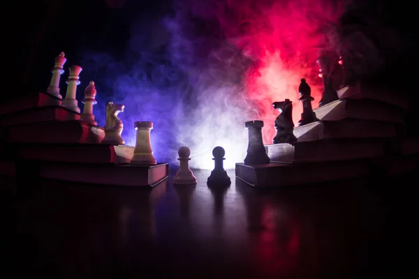 Business hierarchy. Strategy concept with chess pieces. Chess standing on a pyramid of books with the king at the top. Dark foggy background with toned light. Copy space.