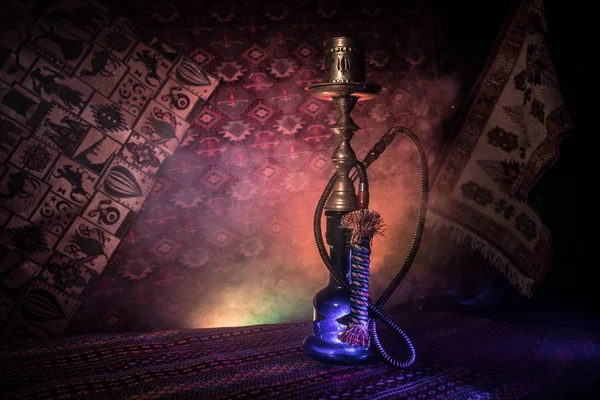 Hookah hot coals on shisha bowl making clouds of steam at Arabian interior. Oriental ornament on the carpet. Stylish oriental shisha in dark with backlight. For Shisha advertisement. Selective focus