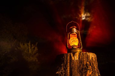 Horror Halloween concept. Burning old oil lamp in forest at night. Night scenery of a nightmare scene. Selective focus. clipart