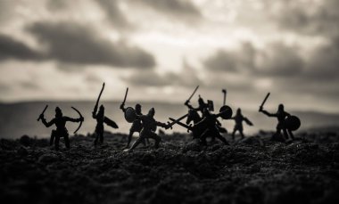 Medieval battle scene with cavalry and infantry. Silhouettes of figures as separate objects, fight between warriors on sunset foggy background. Selective focus clipart