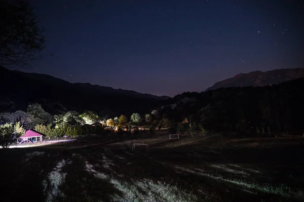 Mountain night landscape of building at forest at night with moon or vintage country house at night with clouds and stars. Summer night. Photo taken with long exposure