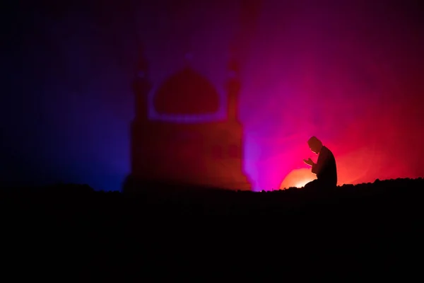 Silhouette of praying man with blurred mosque building on toned foggy background. Ramadan Kareem background. Muslim Eid holiday decoration. Praying people religion concept. Selective focus