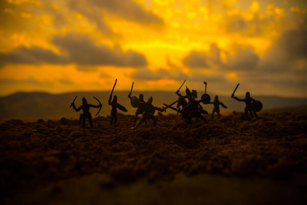 Medieval battle scene with cavalry and infantry. Silhouettes of figures as separate objects, fight between warriors on sunset foggy background. Selective focus