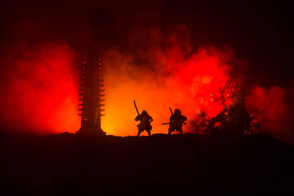 Samurai fighting concept. Silhouette of samurais in duel near tree and old temple. Table decoration with dark toned foggy background. Selective focus
