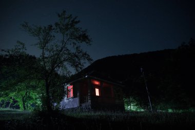 Binanın Orman geceleri ay veya vintage kır evi ile bulutlar ve yıldız ile gece dağ gece manzarası. Yaz gecesi. Uzun pozlama ile çekilen fotoğraf