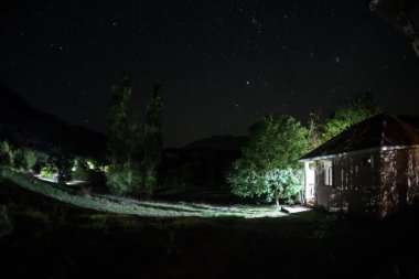 Binanın Orman geceleri ay veya vintage kır evi ile bulutlar ve yıldız ile gece dağ gece manzarası. Yaz gecesi. Uzun pozlama ile çekilen fotoğraf