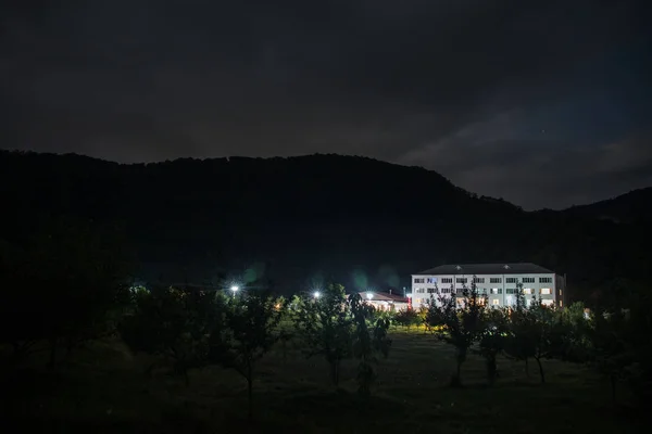 Mountain night landscape of building at forest at night with moon or vintage country house at night with clouds and stars. Summer night. Photo taken with long exposure