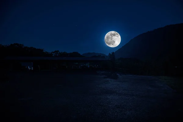 Mountain Road through the forest on a full moon night. Scenic night landscape of dark blue sky with moon