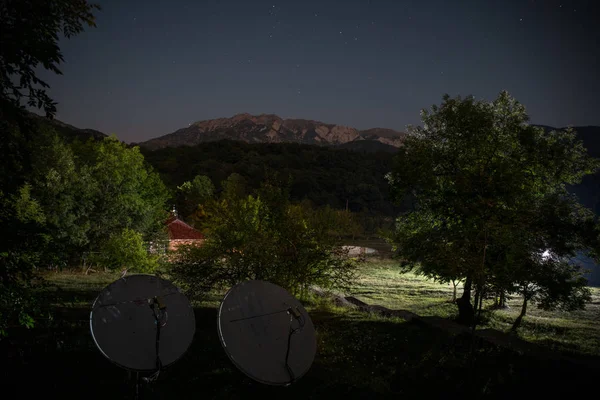 Beautiful night landscape with starry night mountains and forest. Night forest with green meadow and mountains in bright starry night or view of milky way