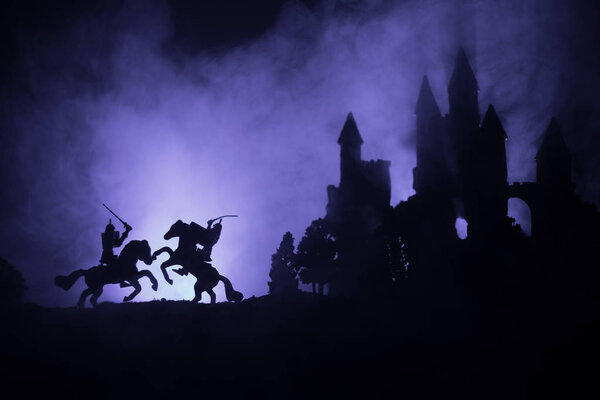 Medieval battle scene with cavalry and infantry. Silhouettes of figures as separate objects, fight between warriors on dark toned foggy background with old gothic castle