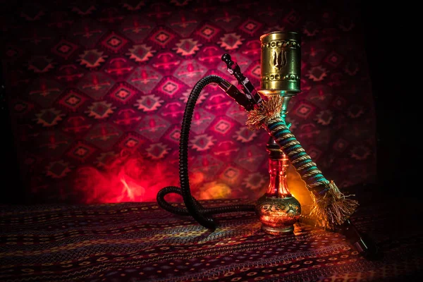 Hookah hot coals on shisha bowl making clouds of steam at Arabian interior. Oriental ornament on the carpet. Stylish oriental shisha in dark with backlight. For Shisha advertisement. Selective focus