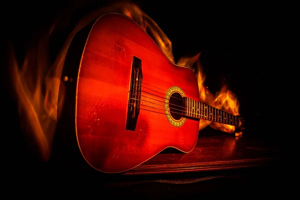 Music concept. Acoustic guitar on a dark background under beam of light with smoke with copy space. Exploding guitar. Fire effects. Surreal guitar. Selective focus