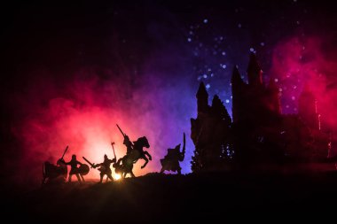 Süvari ve piyadelerle ortaçağ savaş sahnesi. Şekillerin siluetleri ayrı nesneler olarak, karanlık tonlu sisli arka planda ortaçağ şatosuyla savaşan savaşçılar arasında. Seçici odak