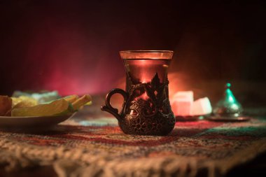 Cam bir halı ile ışık ve duman koyu arka plan üzerinde Doğu snacks ile Arap tea. Doğu çay kavramı. Boş alanı. Seçici odak.