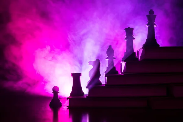 Business hierarchy. Strategy concept with chess pieces. Chess standing on a pyramid of books with the king at the top. Dark foggy background with toned light. Copy space.