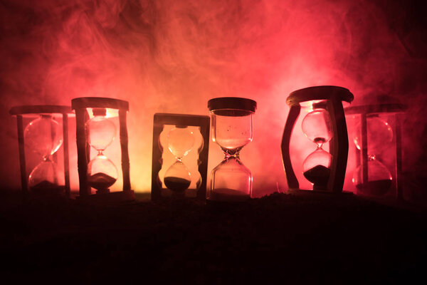 Time concept. Silhouettes of Hourglasses on dark toned foggy background with back lighting. Abstract surreal concept with copy space. Selective focus