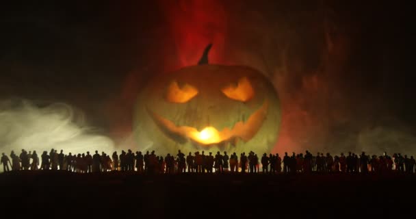 Concept d'Halloween. Silhouette floue de citrouille géante Jack-o-lanterne avec un visage souriant effrayant derrière la foule la nuit. Les gens regardent une grosse citrouille la nuit. Concentration sélective.