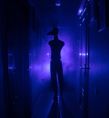 Ürpertici siluet koyu terk edilmiş binada. Korku Cadılar Bayramı kavramı. Karanlık koridor ortasında duran korku kişi silueti ile. Tonda ışık ve sis arka plan üzerinde.