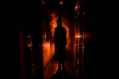 Ürpertici siluet koyu terk edilmiş binada. Korku Cadılar Bayramı kavramı. Karanlık koridor ortasında duran korku kişi silueti ile. Tonda ışık ve sis arka plan üzerinde.