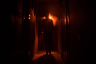 Ürpertici siluet koyu terk edilmiş binada. Korku Cadılar Bayramı kavramı. Karanlık koridor ortasında duran korku kişi silueti ile. Tonda ışık ve sis arka plan üzerinde.