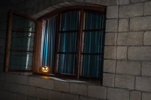 Scary Halloween pumpkin in the mystical house window at night or halloween pumpkin in night on room with blue window. Symbol of halloween in window. Selective focus