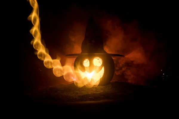 Halloween concept. Jack-o-lantern smile and scary eyes for party night. Close up view of scary pumpkin with witch hat on at dark foggy background. Selective focus. Empty space