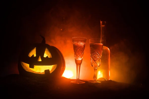 Halloween wine party theme. Two glasses of wine and bottle with Halloween - old jack-o-lantern on dark toned foggy background. Scary Halloween pumpkin