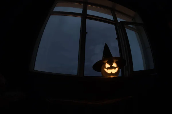 Scary Halloween pumpkin in the mystical house window at night or halloween pumpkin in night on room with blue window. Symbol of halloween in window. Selective focus