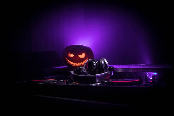 Halloween pumpkin on a dj table with headphones on dark background with copy space. Happy Halloween festival decorations and music concept. Empty space. Selective focus