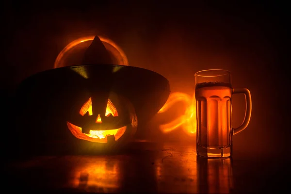 Glass of cold light beer with pumpkin on a wooden table for Halloween. Glass of fresh beer and pumpkin on a dark toned foggy background