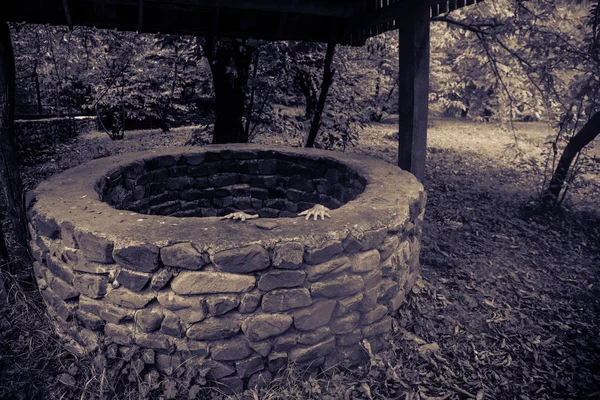 A terrible girl with long black hair is standing in a gloomy well. Scary Halloween photo. Dead zombie girl climbs out of the well