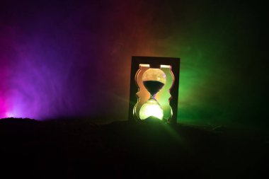 Zaman kavramı. Kum saati saat ve duman sıcak sarı turuncu kırmızı mavi soğuk arka aydınlatma, kopya alanı ile koyu zemin üzerine silüeti. Seçici odak