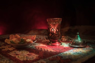 Cam bir halı ile ışık ve duman koyu arka plan üzerinde Doğu snacks ile Arap tea. Doğu çay kavramı. Boş alanı. Seçici odak.