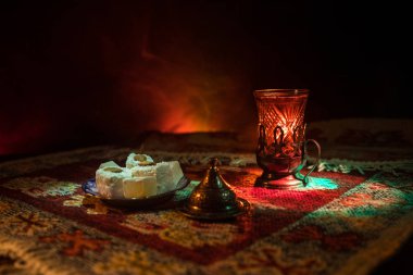 Cam bir halı ile ışık ve duman koyu arka plan üzerinde Doğu snacks ile Arap tea. Doğu çay kavramı. Boş alanı. Seçici odak.