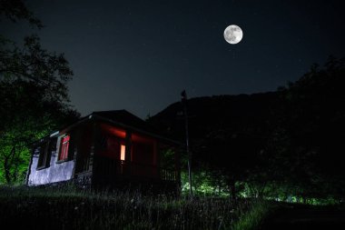 Binanın Orman geceleri ay veya vintage kır evi ile bulutlar ve yıldız ile gece dağ gece manzarası. Yaz gecesi. Uzun pozlama ile çekilen fotoğraf