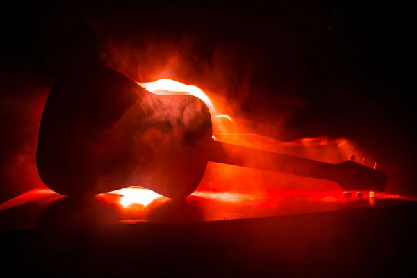 Music concept. Acoustic guitar on a dark background under beam of light with smoke with copy space. Exploding guitar. Fire effects. Surreal guitar. Selective focus