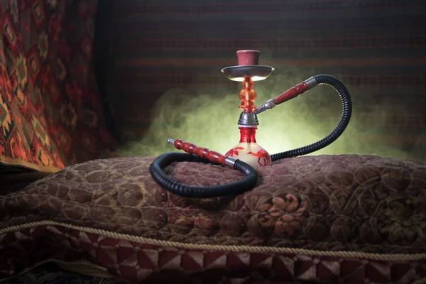 Hookah hot coals on shisha bowl making clouds of steam at Arabian interior. Oriental ornament on the carpet. Stylish oriental shisha with backlight. For Shisha advertisement. Selective focus