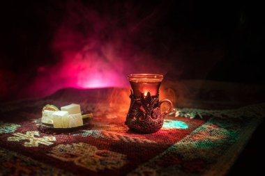 Cam bir halı ile ışık ve duman koyu arka plan üzerinde Doğu snacks ile Arap tea. Doğu çay kavramı. Boş alanı. Seçici odak.