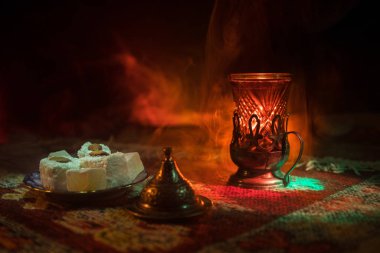 Cam bir halı ile ışık ve duman koyu arka plan üzerinde Doğu snacks ile Arap tea. Doğu çay kavramı. Boş alanı. Seçici odak.