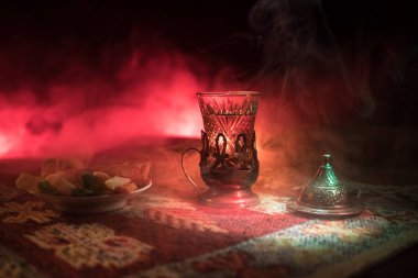Cam bir halı ile ışık ve duman koyu arka plan üzerinde Doğu snacks ile Arap tea. Doğu çay kavramı. Boş alanı. Seçici odak.