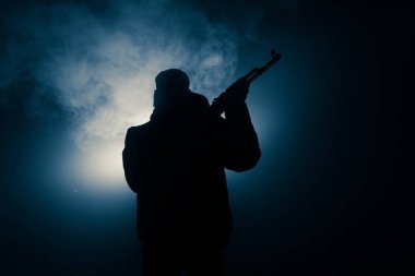 Saldırı tüfeği koyu tonda sisli arka plan veya tehlikeli bir haydut silah elinde tutan saldırmaya hazır olan adam silüeti. Terörist silah Tema dekor ile çekim