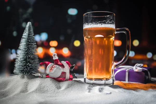 Mug of beer with Christmas decoration. Glass of light beer with foam in snow with creative New Year holiday artwork. Copy space