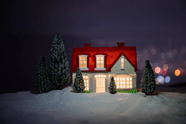 圣诞节和新年微型房子在雪中与冷杉树 小玩具房子在雪与树和 Bokeh 城市灯在背景 圣诞装饰品假期理念 — 图库照片