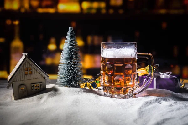 Mug of beer with Christmas decoration. Glass of light beer with foam in snow with creative New Year holiday artwork. Copy space