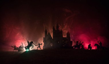 Süvari ve piyadelerle ortaçağ savaş sahnesi. Şekillerin siluetleri ayrı nesneler olarak, karanlık tonlu sisli arka planda ortaçağ şatosuyla savaşan savaşçılar arasında. Seçici odak