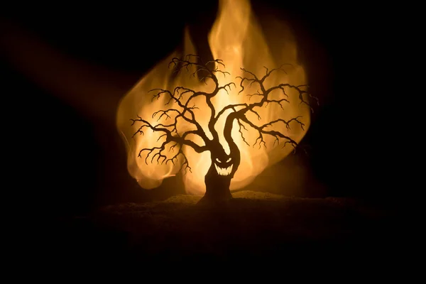 Silhouette of scary Halloween tree with horror face on dark foggy toned fire. Scary horror tree Halloween concept. Selective focus