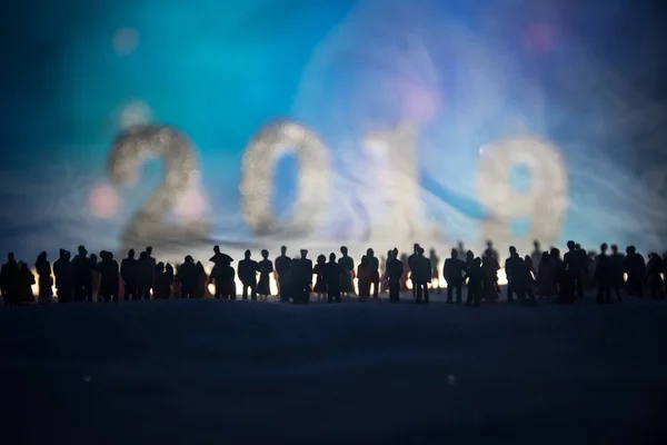 New year or Christmas holiday shopping concept. Store promotions. Silhouette of a large crowd of people watching at a big digits of 2019 year. People on snow ready to shopping. Selective focus