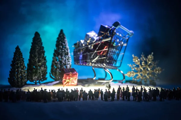 New year or Christmas holiday shopping concept. Store promotions. Silhouette of a large crowd of people watching at a big shopping trolley with gifts. People on snow ready to shopping. Selective focus